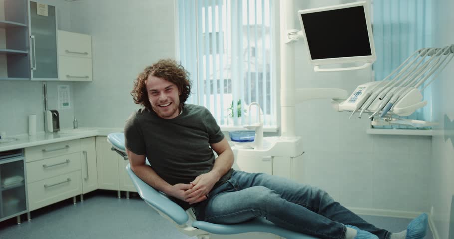 Smiling large young man in the dentist room waiting for his oral check , have a perfect mood showing a big like in front of the camera. 4k