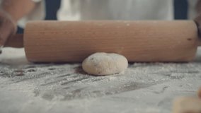 Baker rolls dough with wooden rolling pin. 4K slow motion video