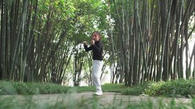 wide angle of One Asian child practice Chinese martial arts in the bamboo woods in the sunny morning, Chinese little girl playing Kung fu in the park, traditional Chinese culture 4k slow motion clips