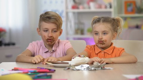 Male and female kids smeared with chocolate sitting table, harmful food sickness