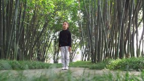 wide angle of One Asian child practice Chinese martial arts in the bamboo woods in the sunny morning, Chinese little girl playing Kung fu in the park, traditional Chinese culture slow motion clips