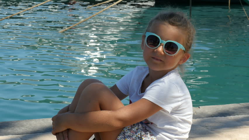 Little pretty girl sitting on seaside and looks at camera.