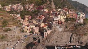 Manarola, Italy. The drone flies over the water, removes the city, colored houses that stand on the mountain. No color correction video with a drone.