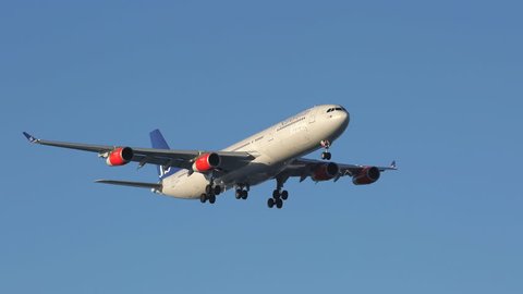 Oslo Airport Norway - ca March 2019: scandinavian airlines sas huge airplane airbus a340 super slow motion passing by panning right blue sky