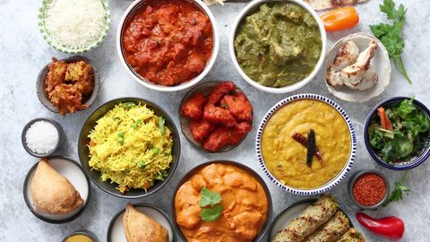 Traditional Indian food in ceramic bowls. Different kind of dishes served with fresh vegetables, rice and naan bread. Flat lay.