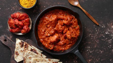 Traditional Indian chicken tikka masala spicy curry meat food in cast iron pan served with naan bread and spices. Flat lay. Top view.