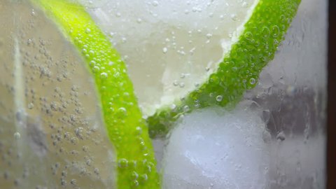 Macro close-up refreshing cold cocktail with lime. soda water covered with bubbles. Slice of lemon with bubbles. 4K UHD video