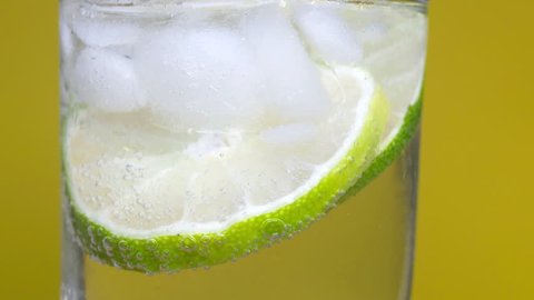Macro close-up, refreshing cold cocktail with lime. soda water covered with bubbles. 4K UHD video