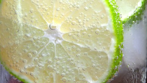 Macro close-up refreshing cold cocktail with lime. soda water covered with bubbles. Slice of lemon with bubbles. 4K UHD video