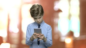 Attractive caucasian boy using smartphone. Cute child boy in shirt surfing internet or watching video on digital gadget. Brown blurry background.