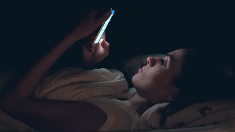Woman use of mobile phone and lying on bed at night. slowmotion.