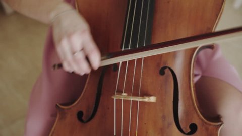 Close view of female violoncellist playing on the strings with fiddlestick. 4K