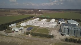 The view from the height of a large farm located among the green hilly fields. Video from a drone or a quadro. Agro-industrial complex with stainless steel silo. Organic food production.Dairy industry