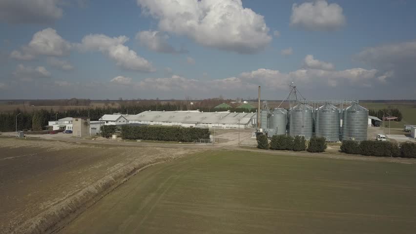The view from the height of a large farm located among the green hilly fields. Video from a drone or a quadro. Agro-industrial complex with stainless steel silo. Organic food production.Dairy industry