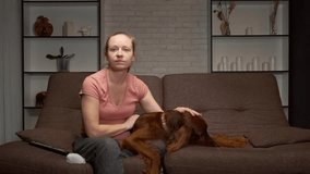 woman strokes a dog's head and watches TV sitting on the sofa at home