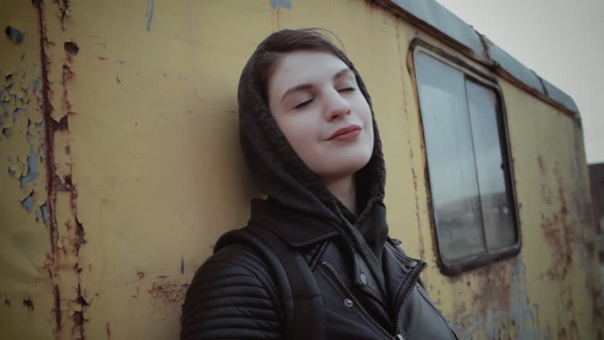 Portrait of young attractive hipster girl in hoodie standing near yellow rusted wall