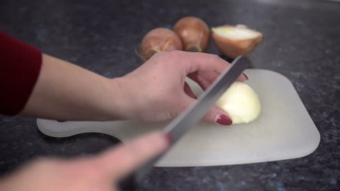 Hands holding sharp knife and chopping fresh onion on kitchen board