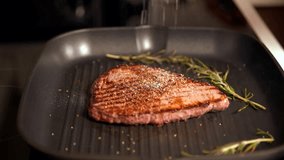 Cook adding seasoning and spices to cooking steak