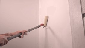Person painting a white wall with a long roller