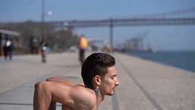 Athletic bare-chested man training at riverside. Side view of shirtless young sportsman exercising on embankment at sunny day, handheld shot. Working out concept