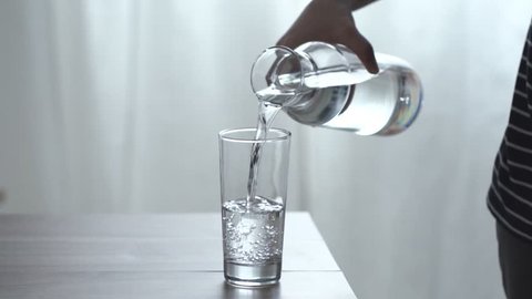 Woman's hand pouring fresh pure water from bottle into a glass on the table, health and diet concept, Slow motion footage