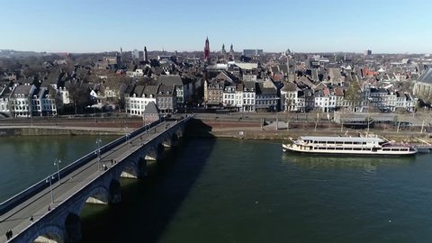 Low altitude aerial view of Sint Servaasbrug is an arched stone footbridge across the Meuse River in Maastricht Netherlands and the oldest bridge in Holland also showing cityscape in background 4k