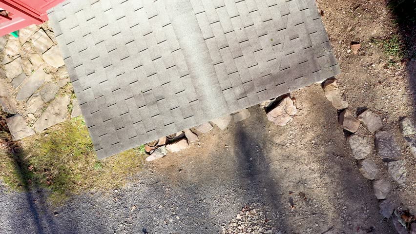 Looking straight down on a house roof and dirt driveway a runner runs out of the house and up the dirt road as the camera ascends way above the leafless trees.