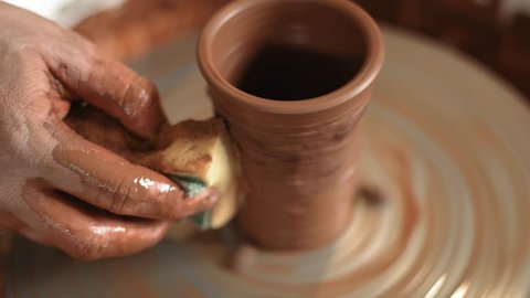 Close up of hands working clay on potter's wheel. The potter makes an authentic pattern using potter's tools on a potter's wheel, raft factory authentic