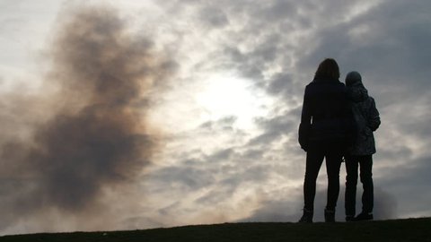  Impressive back view of slender woman in jacket and jeans hugging her son and looking at splendid cloudy sky with dark blurs in spring in slo-mo