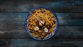 Pilaf on plate with oriental ornament. Central-Asian cuisine - Plov. Rotates on wooden background. Top view