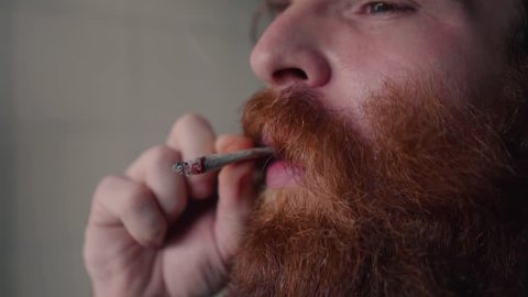 Bearded man smoking close up slow motion rotation rotating slowly with smoke billowing from hand rolled marijuana tobacco cigarette
