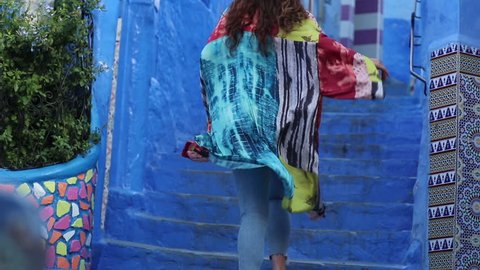 Young women running up stairs in the beautiful Village Chefchaouen in Morocco. Shot in Slowmotion. Wearing a beautiful colored Coat.