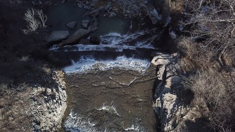 Aerial drone flight over a small waterfall on a sunny day.