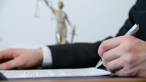 Close up hand of lawyer signing contract with pen at work table in lawyer office. Male hand signing document on justice goddess statue background in law firm