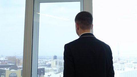 Back view businessman looking to winter city from window in business office. Office worker standing on window background and looking to city panorama