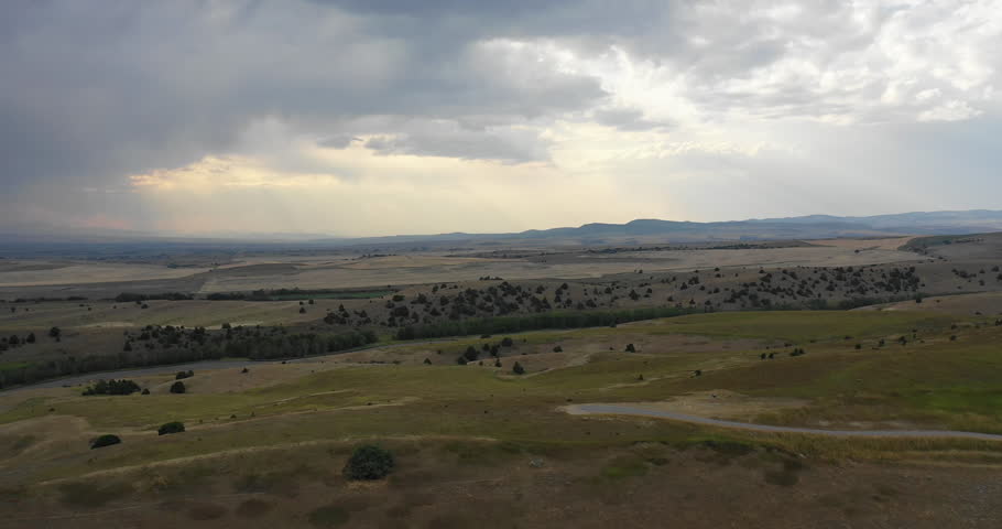 Aerial drone shot above hilly fields. Light shining through big open sky clouds above beautiful rural countryside of Montana in 4k.