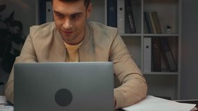 attentive businessman using laptop while sitting at workplace in office at night