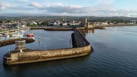 Medieval Norman Castle and harbor in Carrickfergus near Belfast in sunrise light. Aerial 4K flyby video with water reflection, marina, breakwater and town