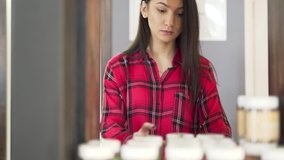 It is video with blurred background. Pretty girl in red and black checked shirt is concentrated on reading ingredients list on hair mask she has just taken from shelf. Quality attracts her attention