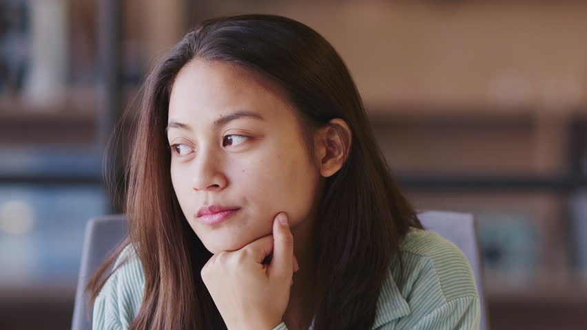Millennial Asian female creative looking way in contemplation, resting chin on hand, close up | Shutterstock HD Video #1026274541
