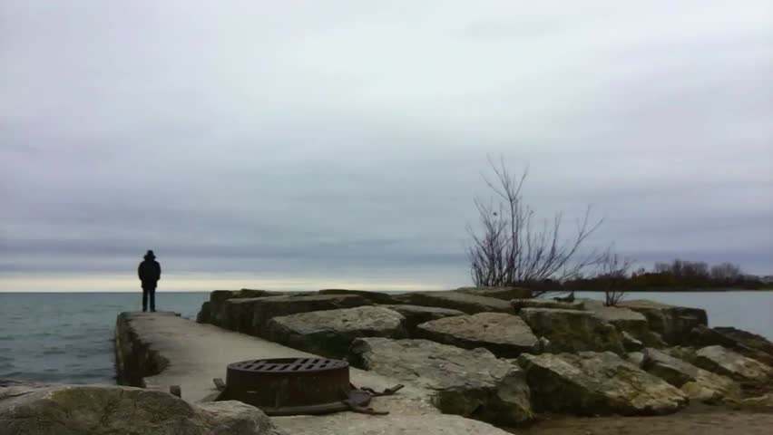 Solitary man, looking into the distance, at the end of a small concrete pier jutting out into a lake