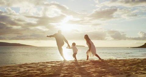 Happy family jumping and running toward the ocean on the beach at sunset, island family lifestyle