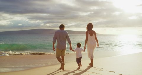 Happy mom and dad with small toddler son walking on the beach at sunset, island family vacation