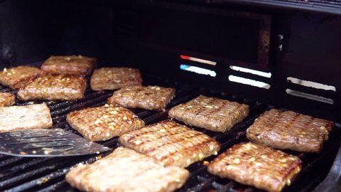 Flipping a Dozen Square Cheddar Stuffed Hamburgers on a Flaming Hot Grill with a Slotted Spatula, Shallow Focus