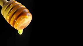 Honey dripping from honey dipper over black background. Healthy organic Thick honey dipping from the wooden honey spoon. 4K UHD video footage 3840X2160. Isolated On black background