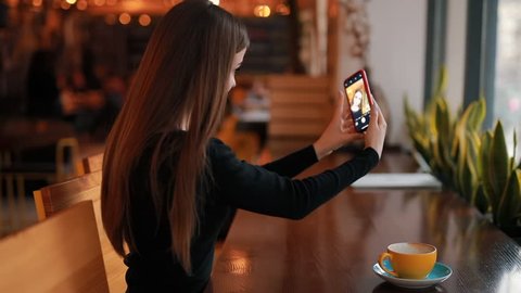 Woman blogger photographing cup of coffee for her social account sitting in cafe