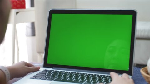 Over the shoulder shot of Asian woman looking at green screen. Office person using laptop computer with laptop green screen, 4K dolly shot