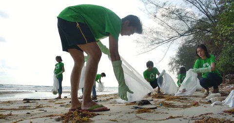 Group of young asian people volunteers in green t-shirts cleaning up the beach with plastic bags full of garbage. Safe ecology concept. 4k resolution.