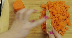Female housewife hands slicing carrots into pieces on the wooden cutting board in the kitchen