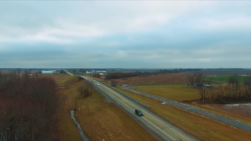 Cars, trucks and a bus traveling across an overpass running over railroad tracks next to a pond on a rural Illinois highway.